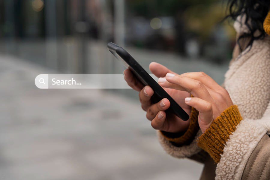Mujer abrigada sosteniendo un smartphone y haciendo uso de Google para realizar una búsqueda en Internet.